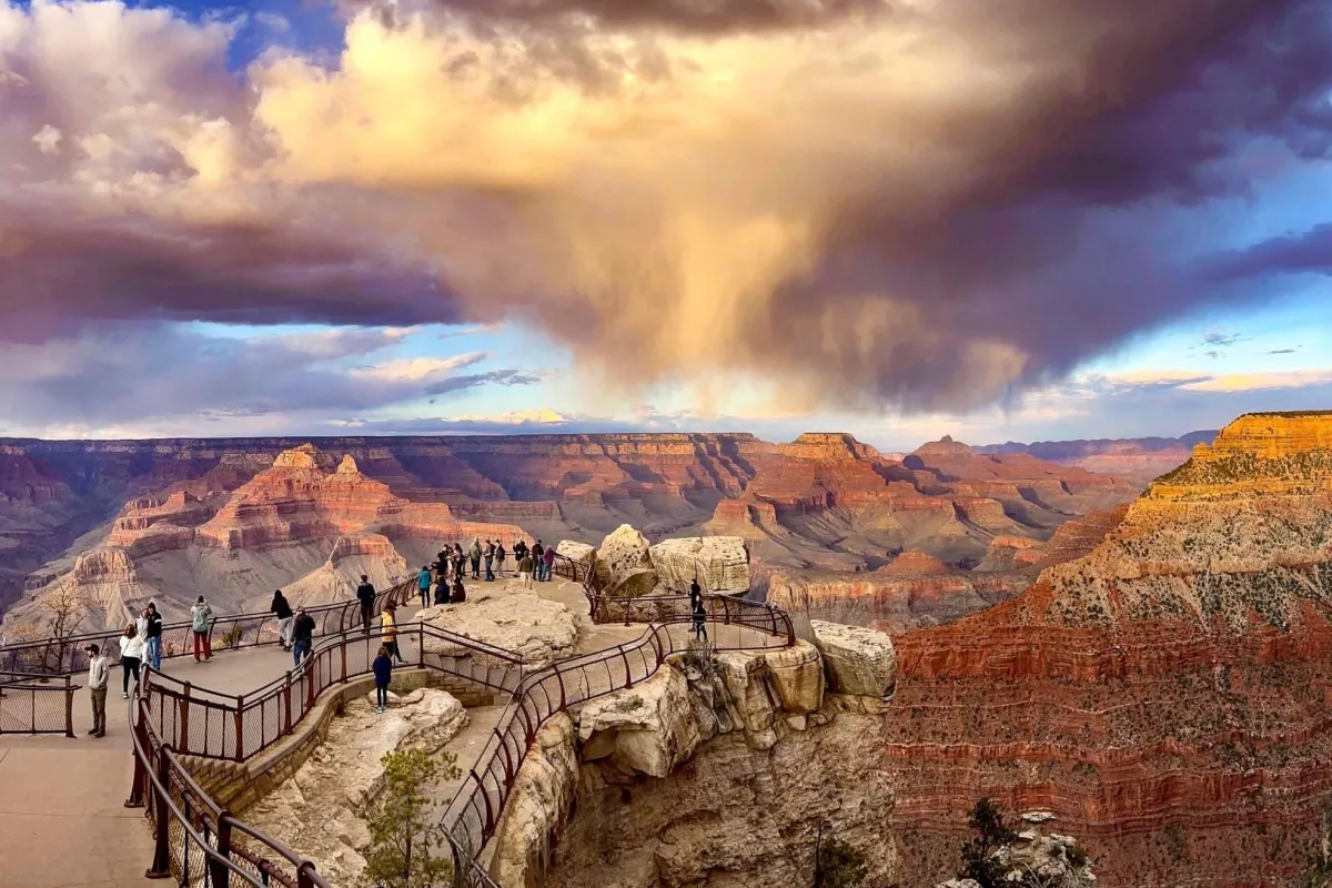 At Sunset, swirling rain clouds above a vast canyon filled with colorful peaks and cliff walls.