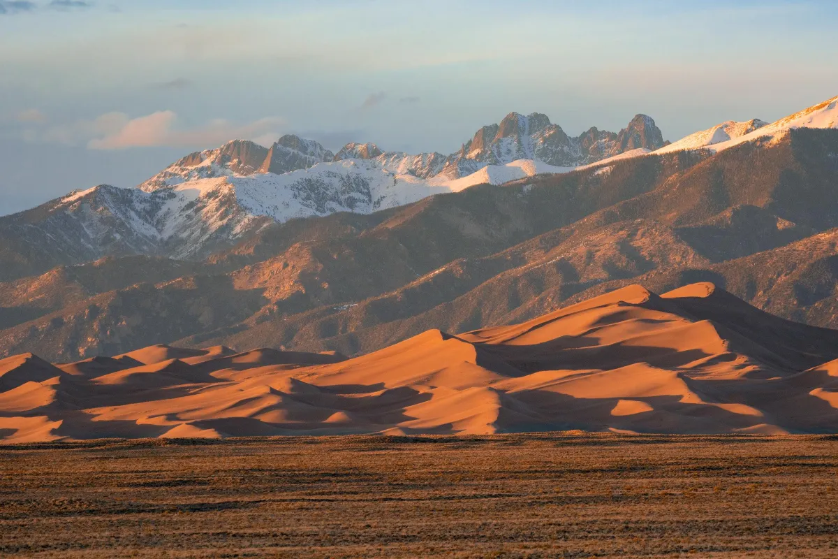 Grasslands, large dunes, and snow-capped peaks at sunset