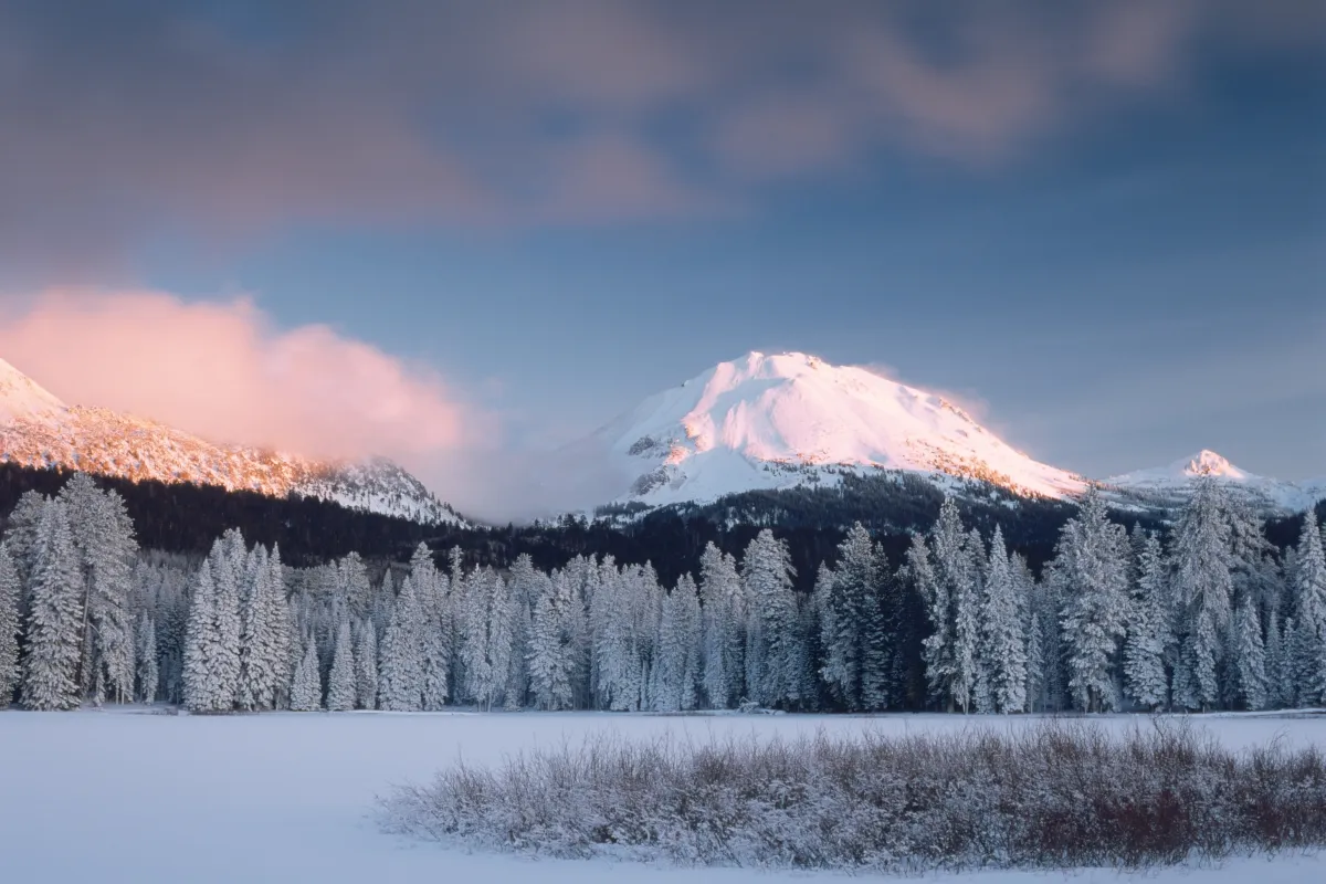 A frozen lake below snow-covered trees and peak