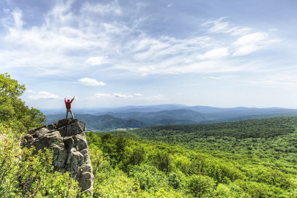A man stands on a rocky outcrop overlooking the receding mountains.