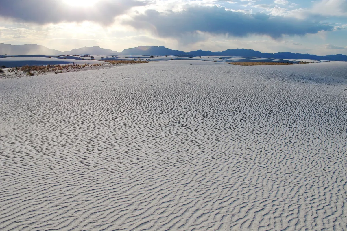 White dunes in foreground with sun setting behind mountain.