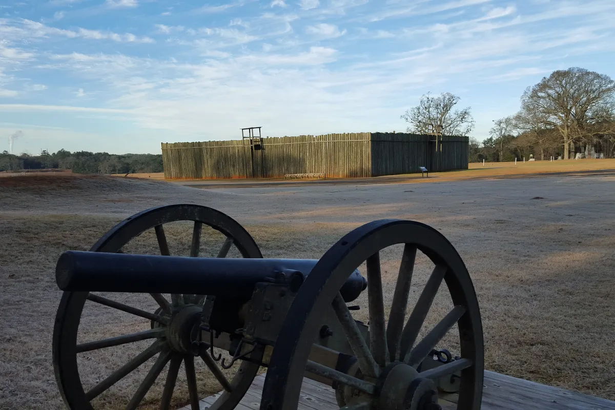 A cannon sits out in front of a replica of part of the wooden stockade walls once at Andersonville