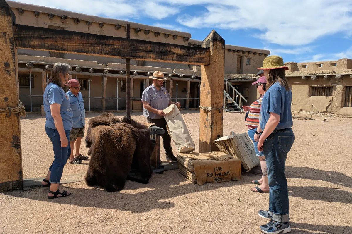 A group of visitors stand around a large wooden apparatus in a plaza courtyard.