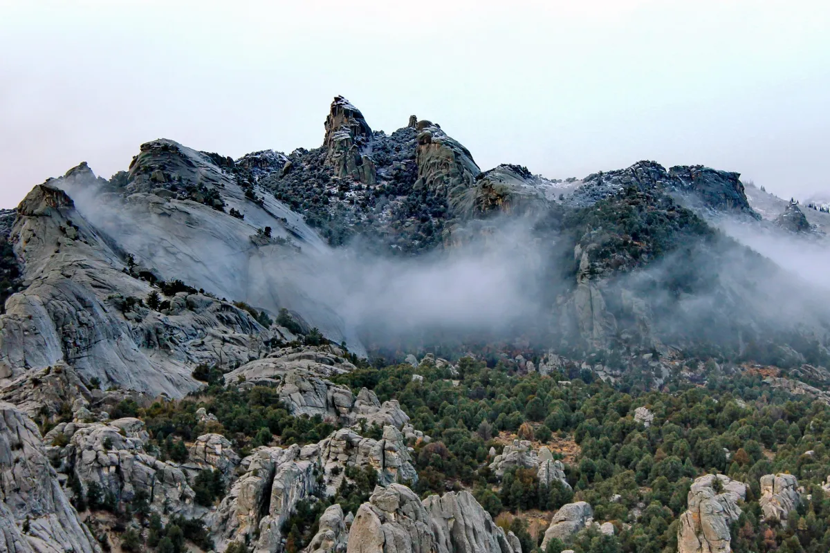 Snow dusted granite formations jut up from a mountainous juniper covered landscape.