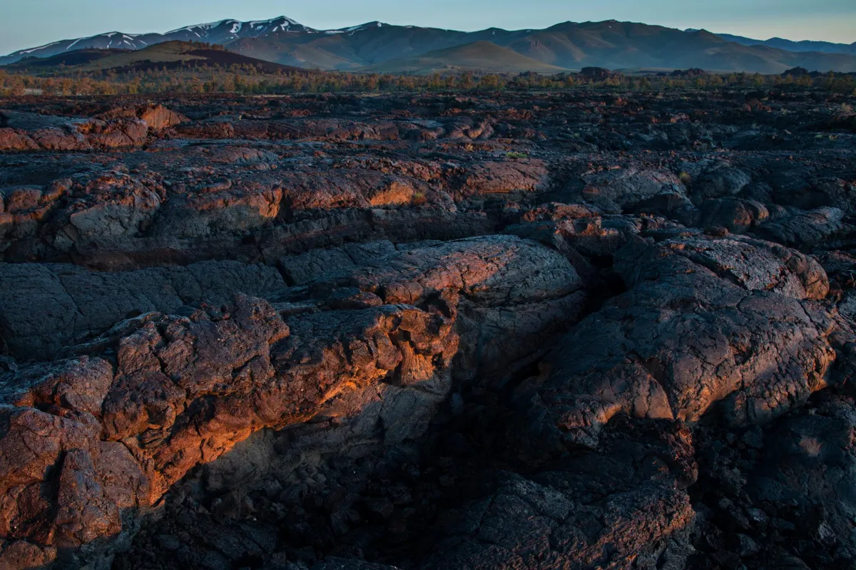 A close-up shot of a folded, waving sea of lava rock, with mountains in the far distance.
