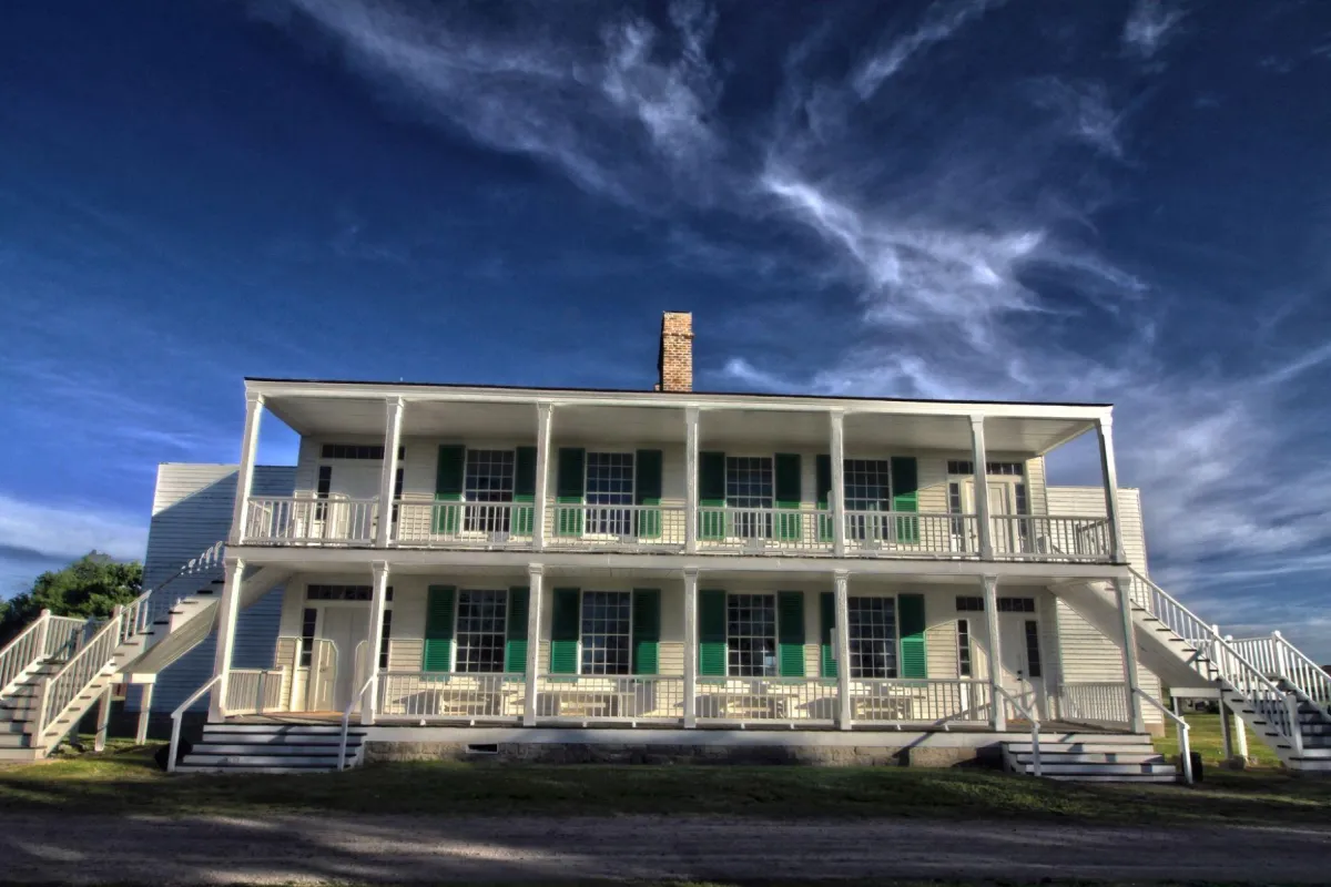 A large two story white building with pillars. Several windows with green shutters