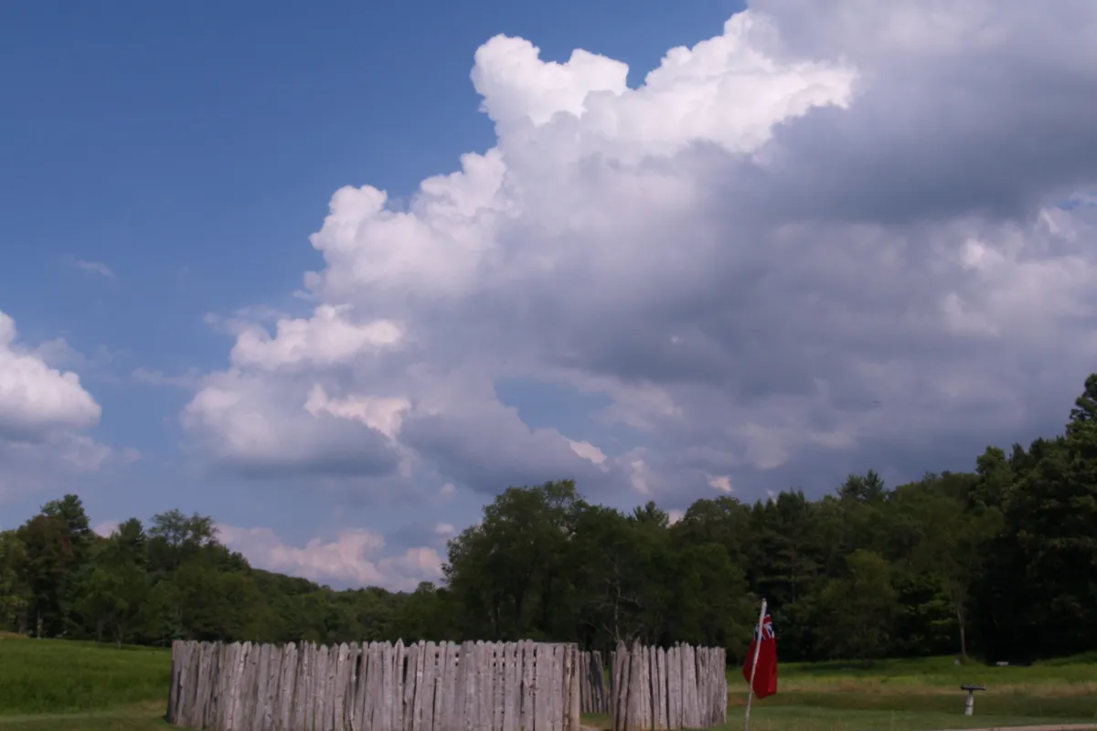 Circular stockade in the middle of a meadow. Dramatic clouds build in the blue sky.