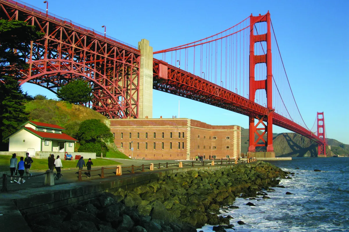 Fort Point with visitors approaching on road in front and Golden Gate Bridge above.