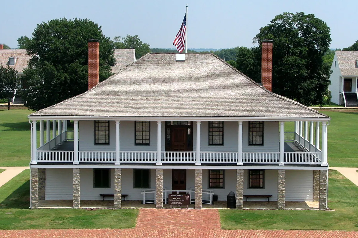 Picture of the post hospital with the parade ground and trees in the background.