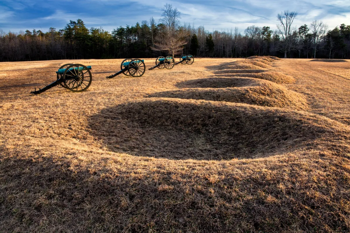 A line of four cannons placed in front of crescent shaped earthen gun pits.