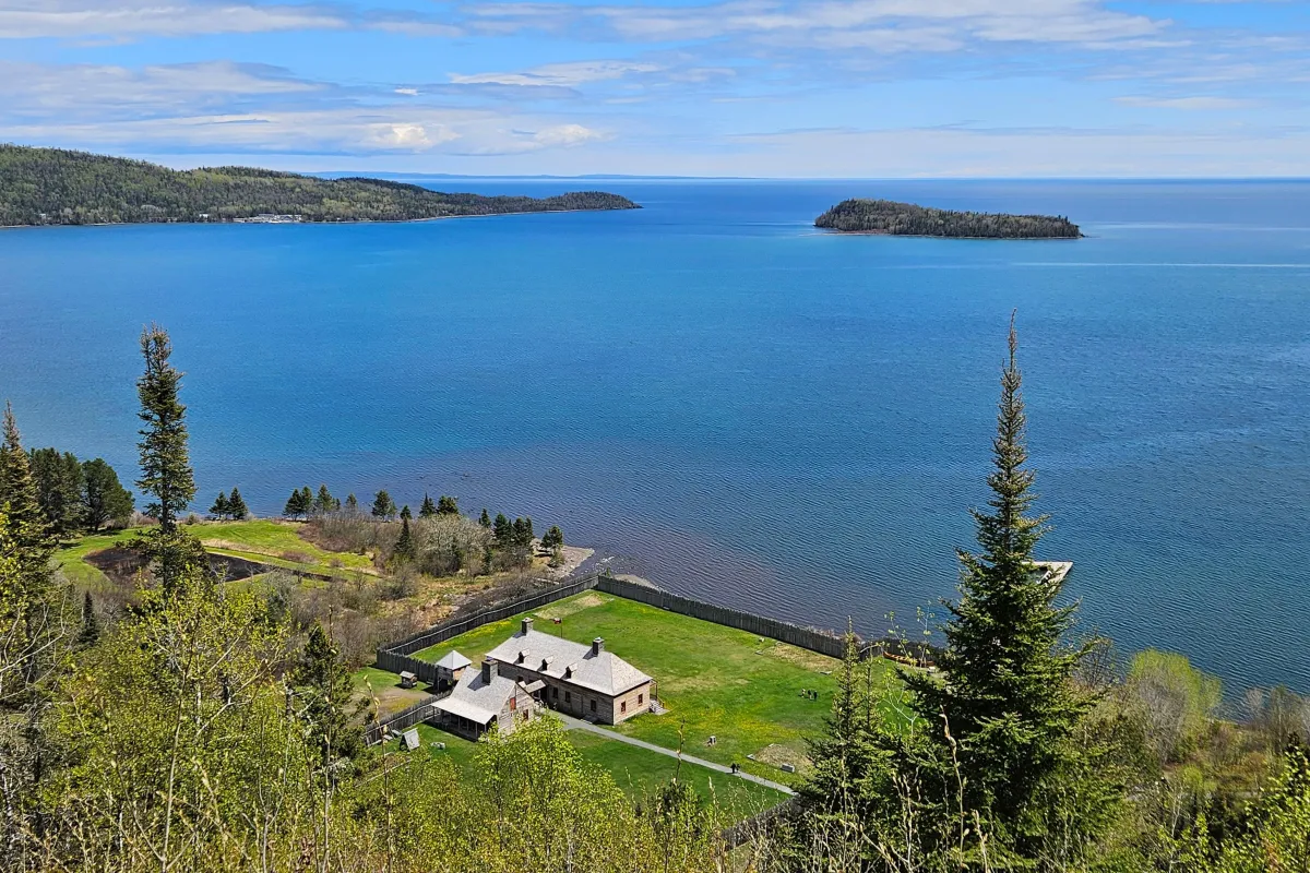 Log buildings, stockade fence and dock near a large lake.