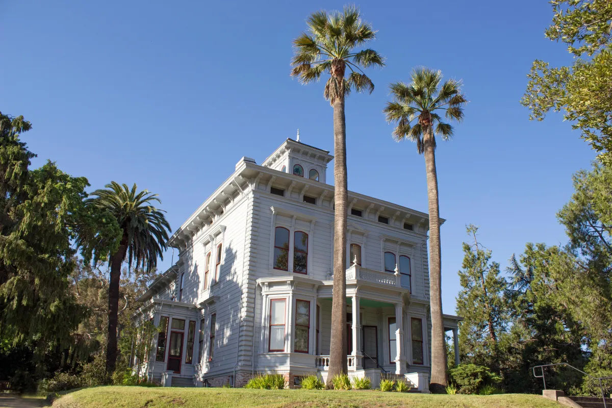 White two story house capped by a bell tower and ringed with palm trees