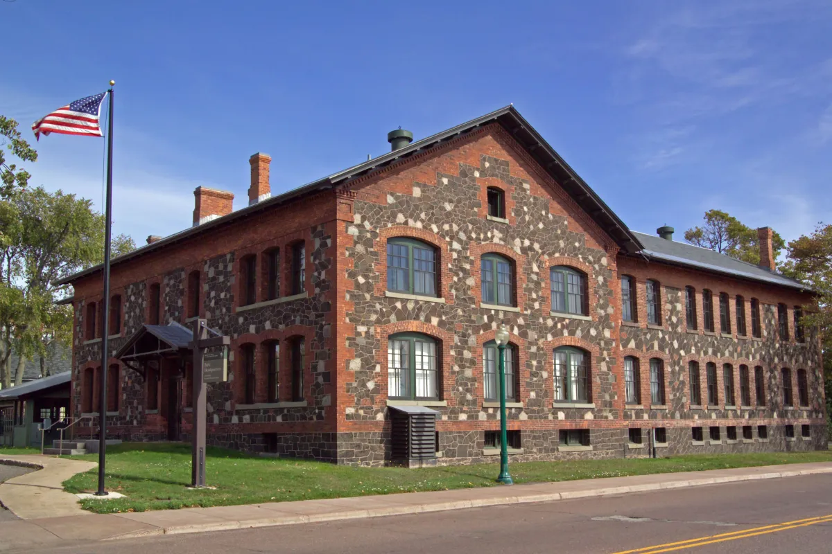 Two story stone and brick building. The American flag flies in front of a blue sky background