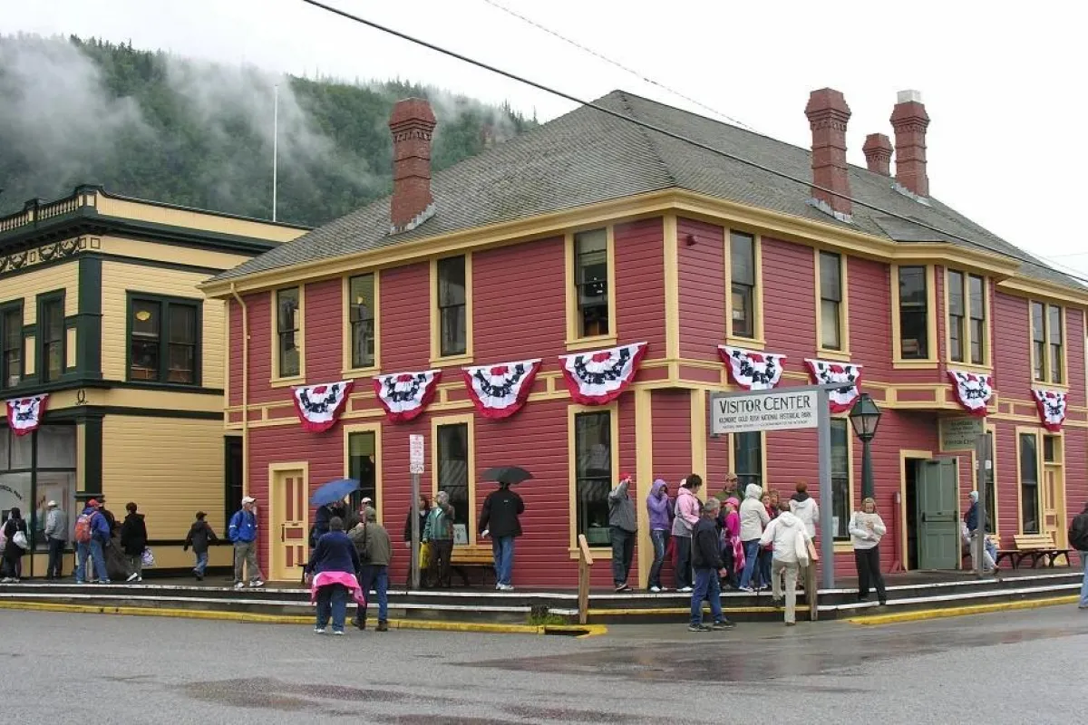 Visitors stand on a boardwalk outside a brick red colored wooden building with tidy golden trim.