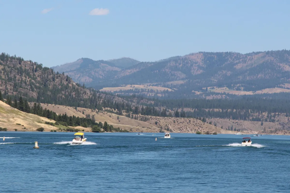 Various motorboats on a blue lake, landscaped by tall tree filled hills.
