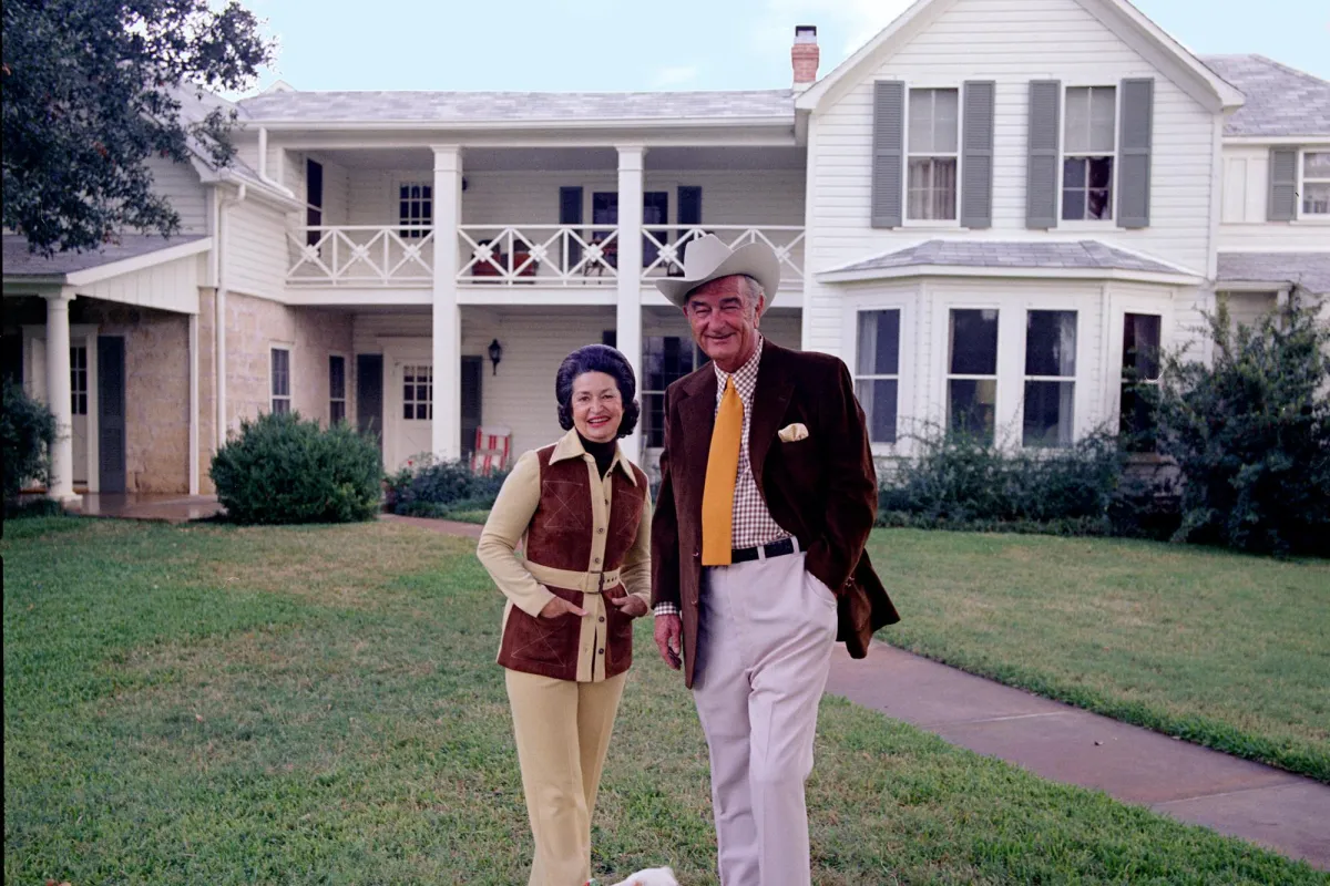 President and Mrs. Johnson stand with their small, white dog in front of the Texas White House.