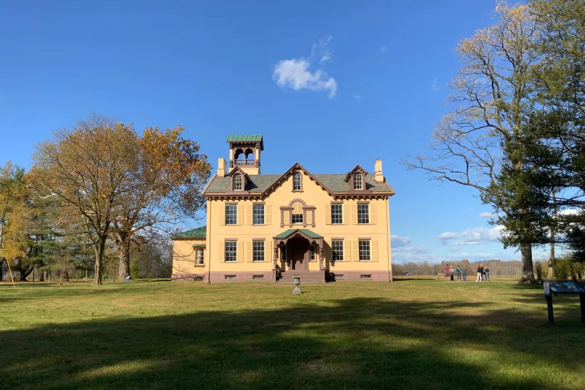 Lindenwald, a yellow, 3 story mansion, is surrounded by trees.