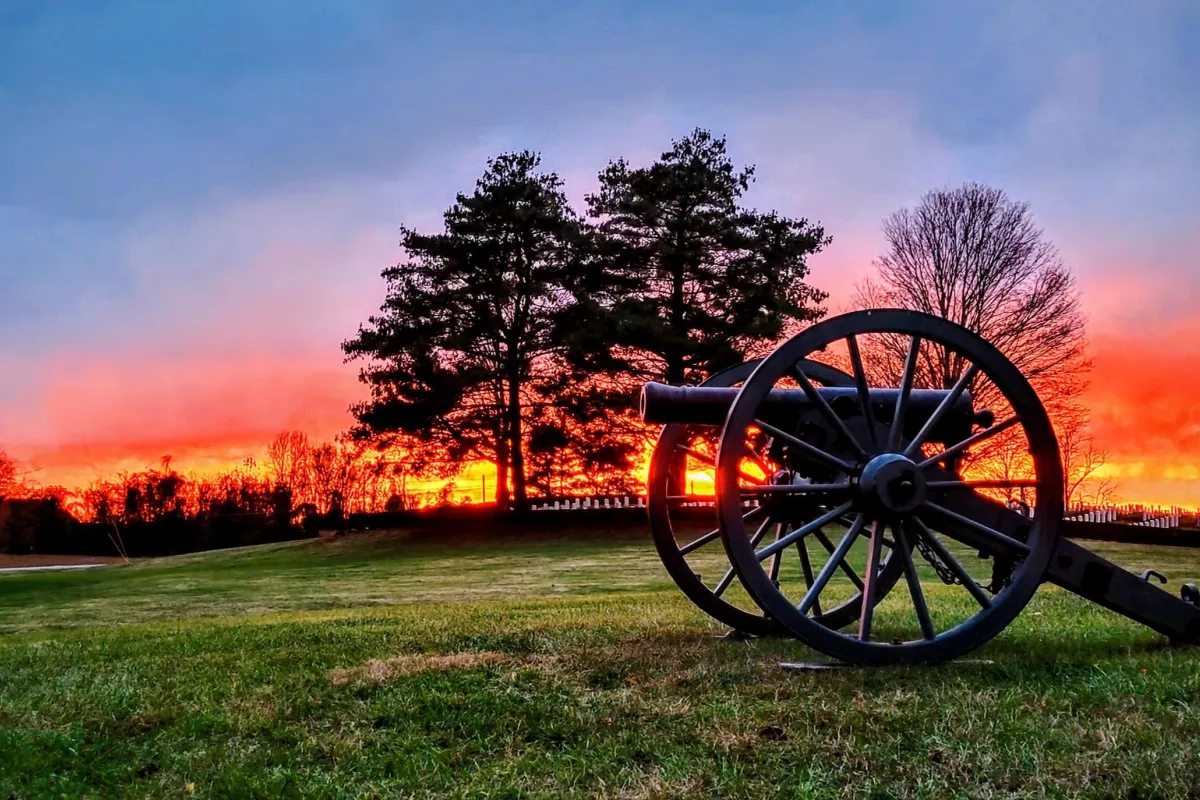 A orange sunset over the white granite headstones in the national cemetery with silhouetted cannon.