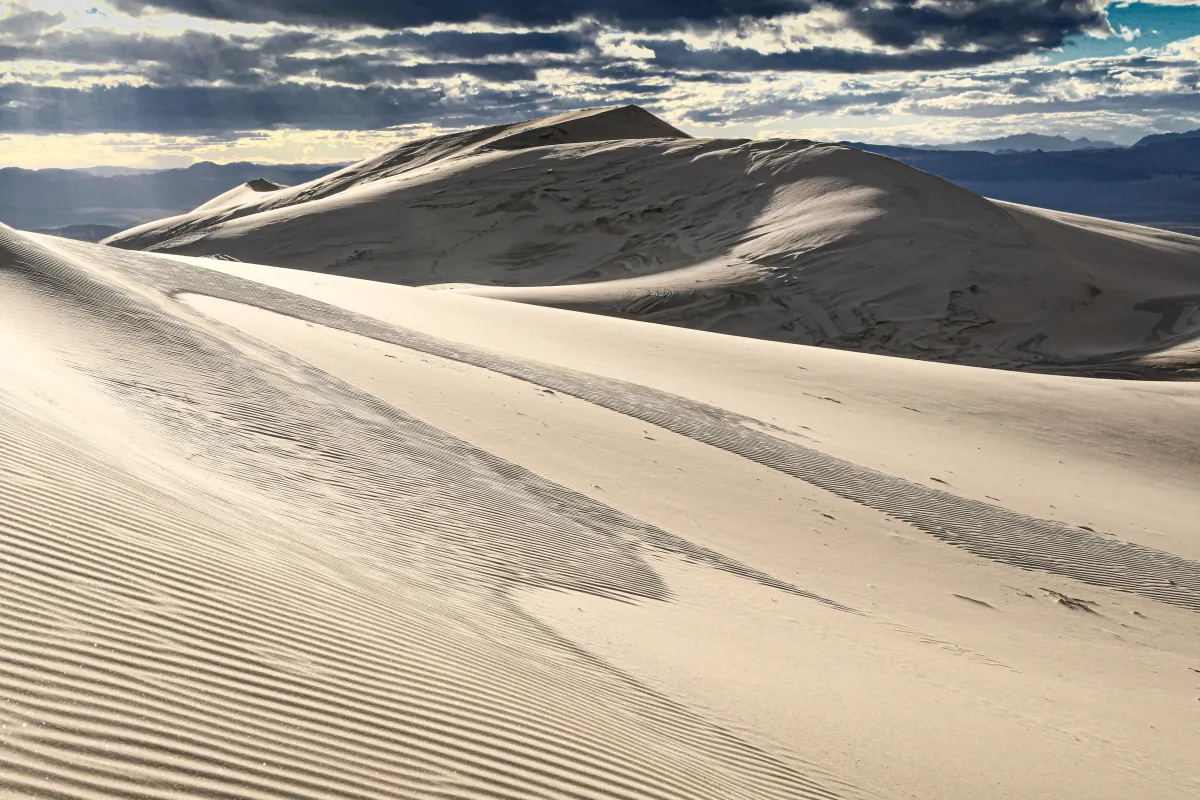 Kelso Dunes with rays of light coming through the clouds. Mountains in the background..