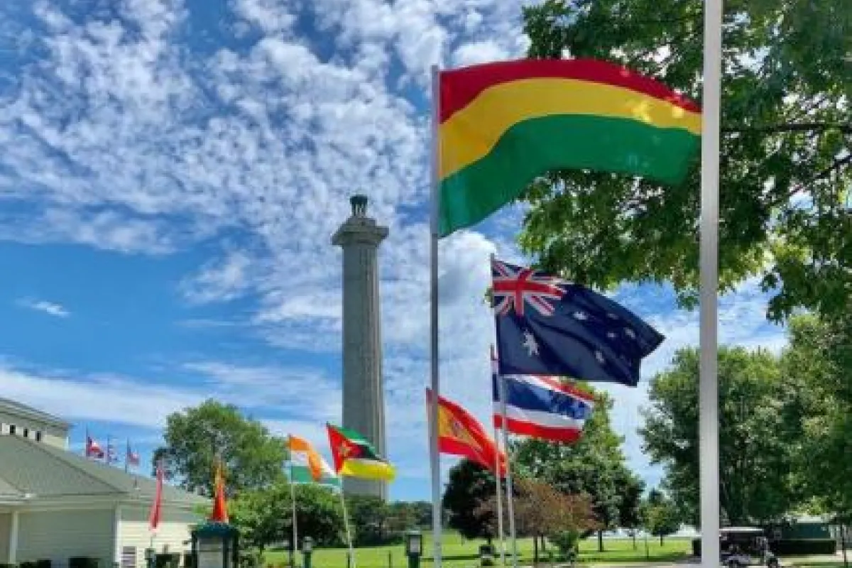 9-3'x5' international flags line sidewalk that leads to a white building with green roof. Tall stone