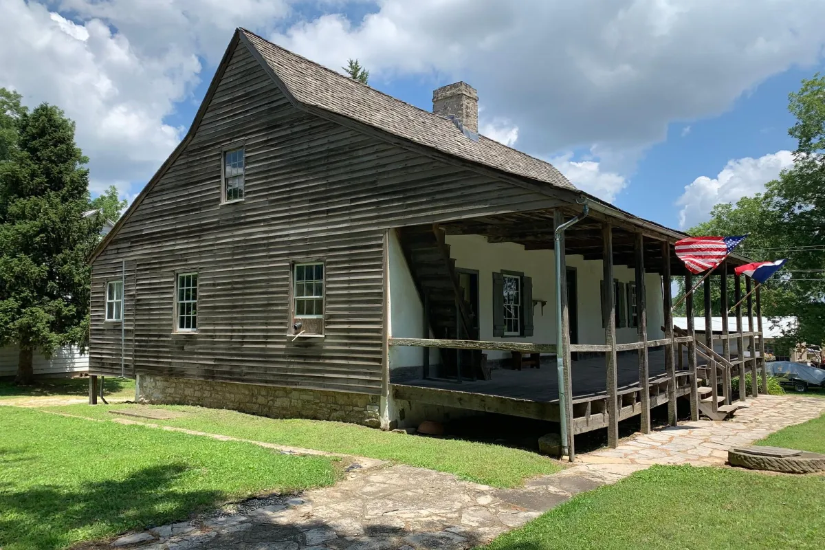 Frame house made of wood with U.S. and French flags flying on front porch.