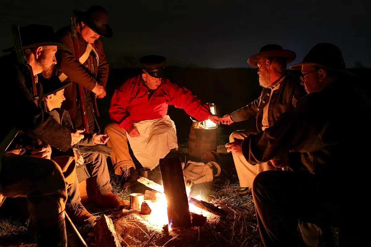 Men in reproduction uniforms talk around a campfire