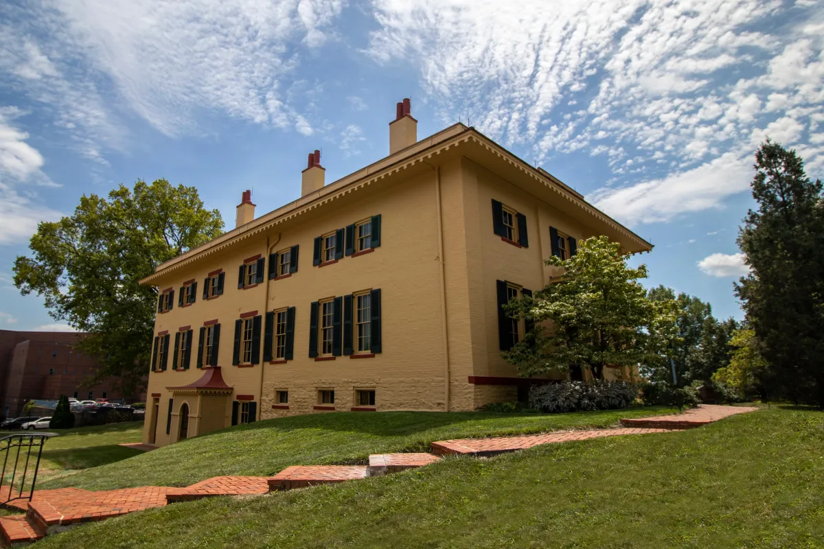 A yellow two-story brick building with tall windows and green shutters on them