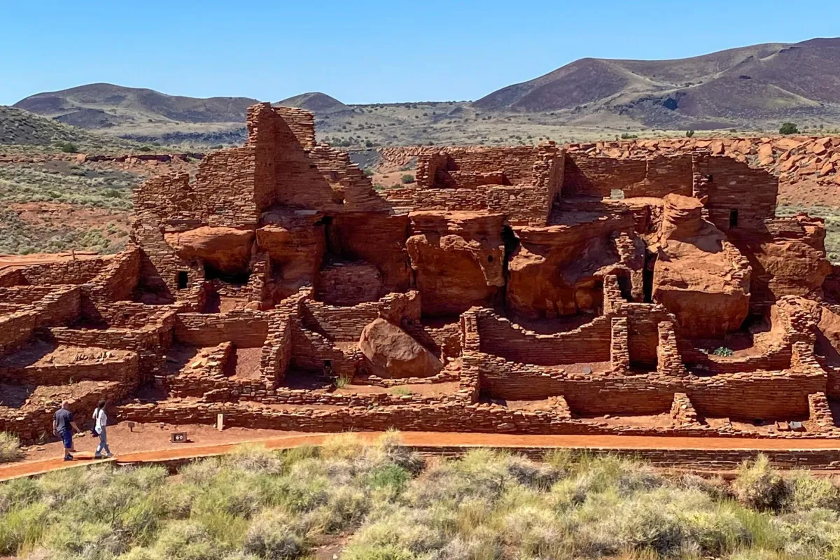 a large stone pueblo in a desert beneath mostly sunny skies with mountains in background